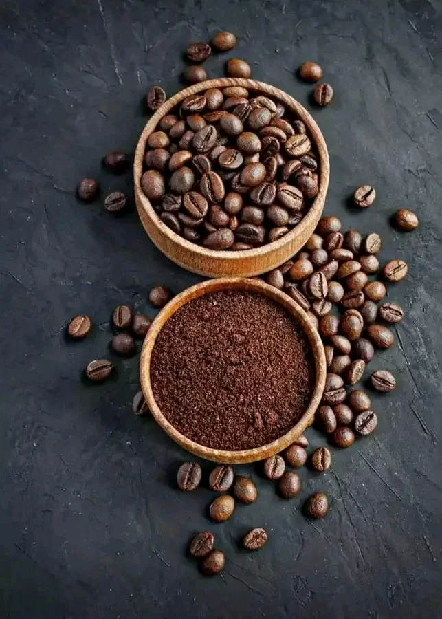 Two wooden bowls of whole roasted coffee beans and ground coffee