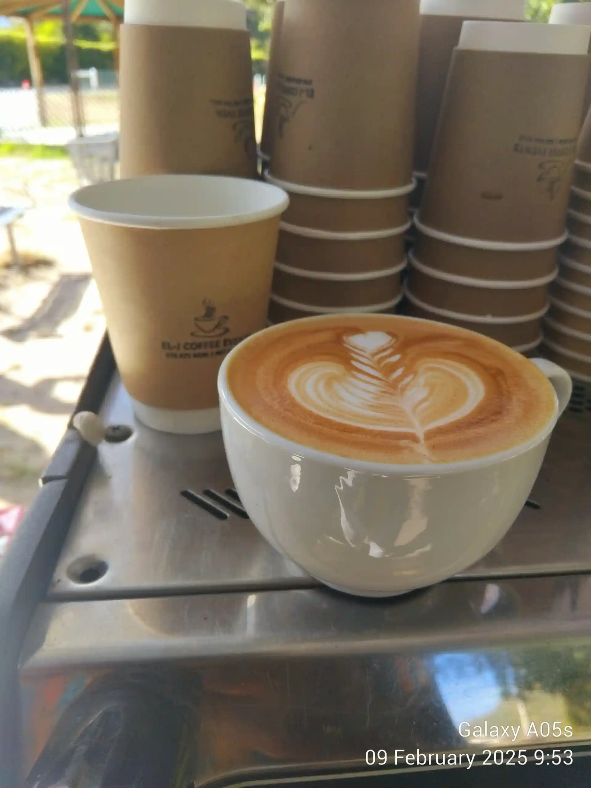 EL-J Coffee branded cups stacked with fresh latte in foreground