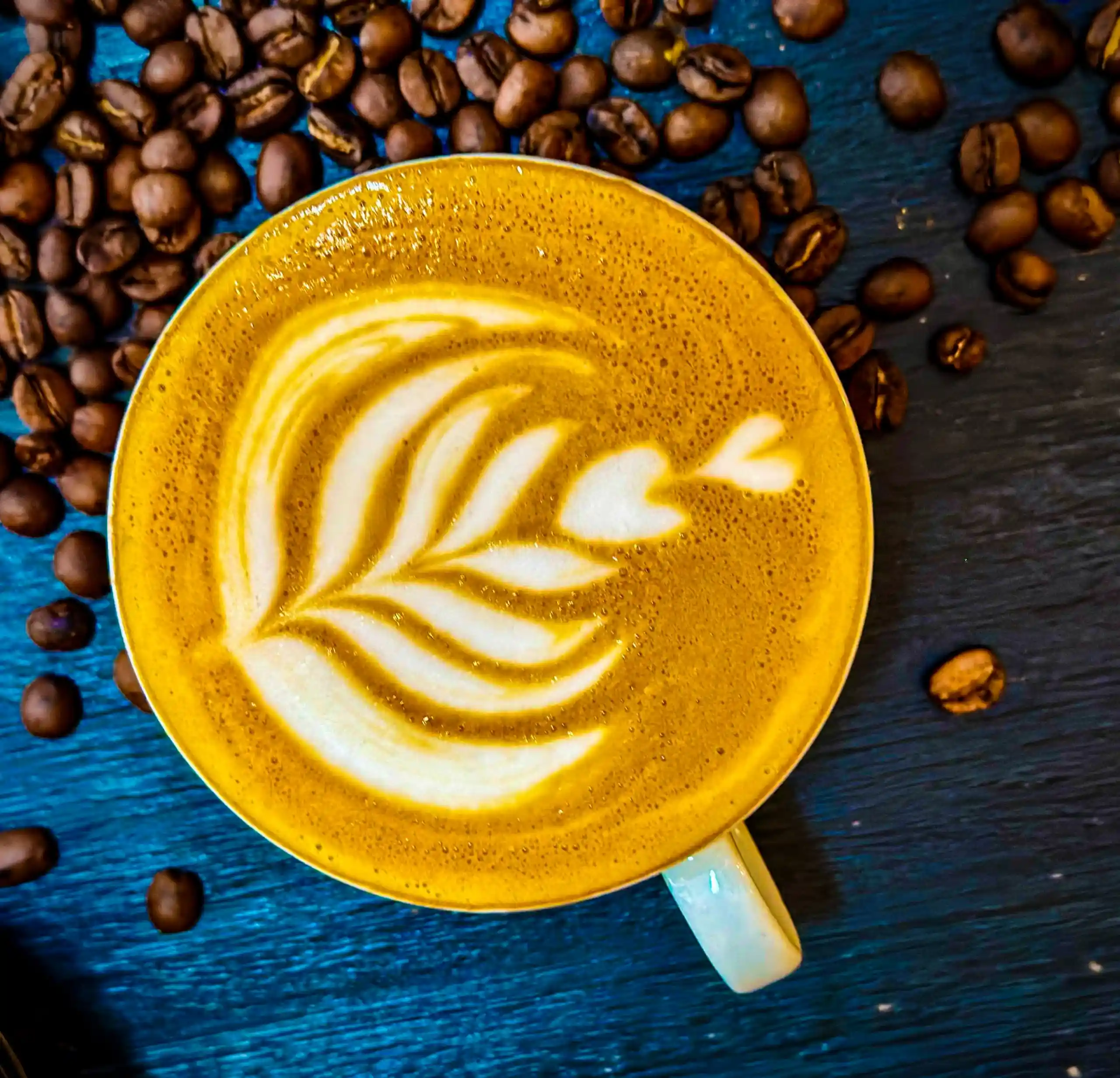Overhead view of latte in a vibrant blue cup with scattered beans