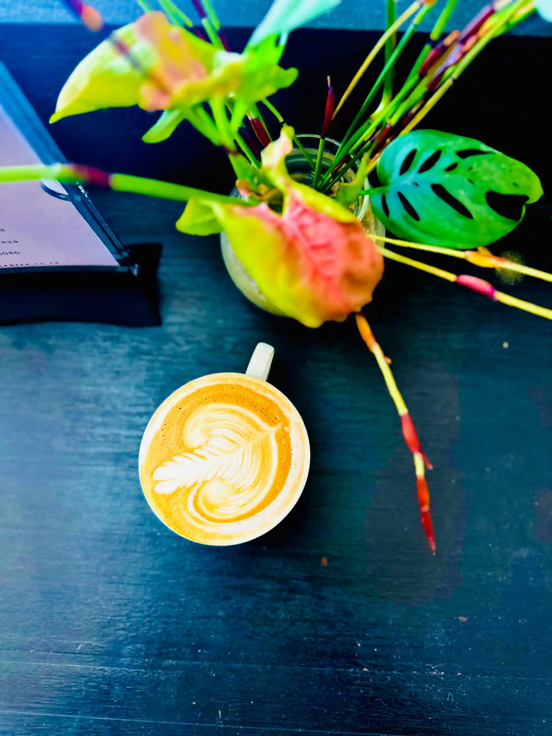 Delicate latte art beside a vase of tropical flowers