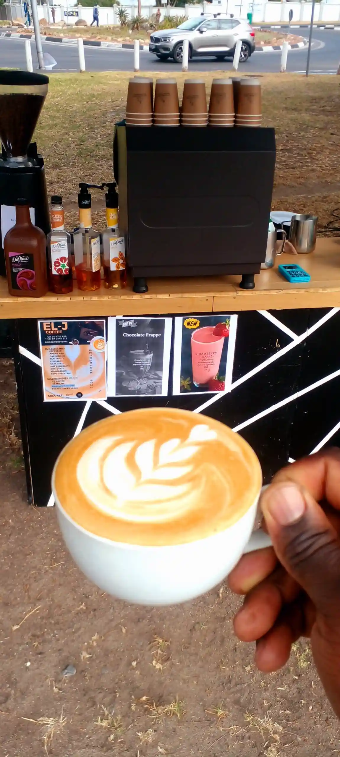 Latte art beside a small glass vase of fresh flowers