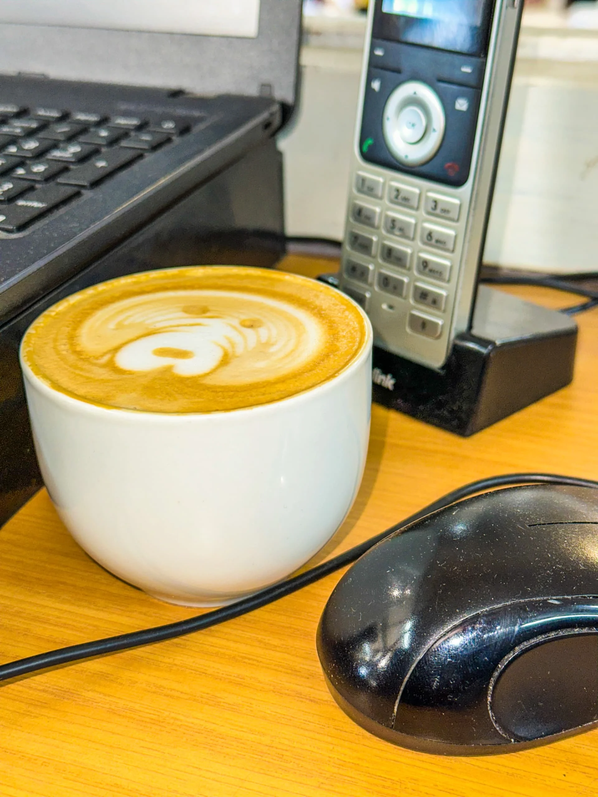 Latte art on an office desk next to a computer and phone