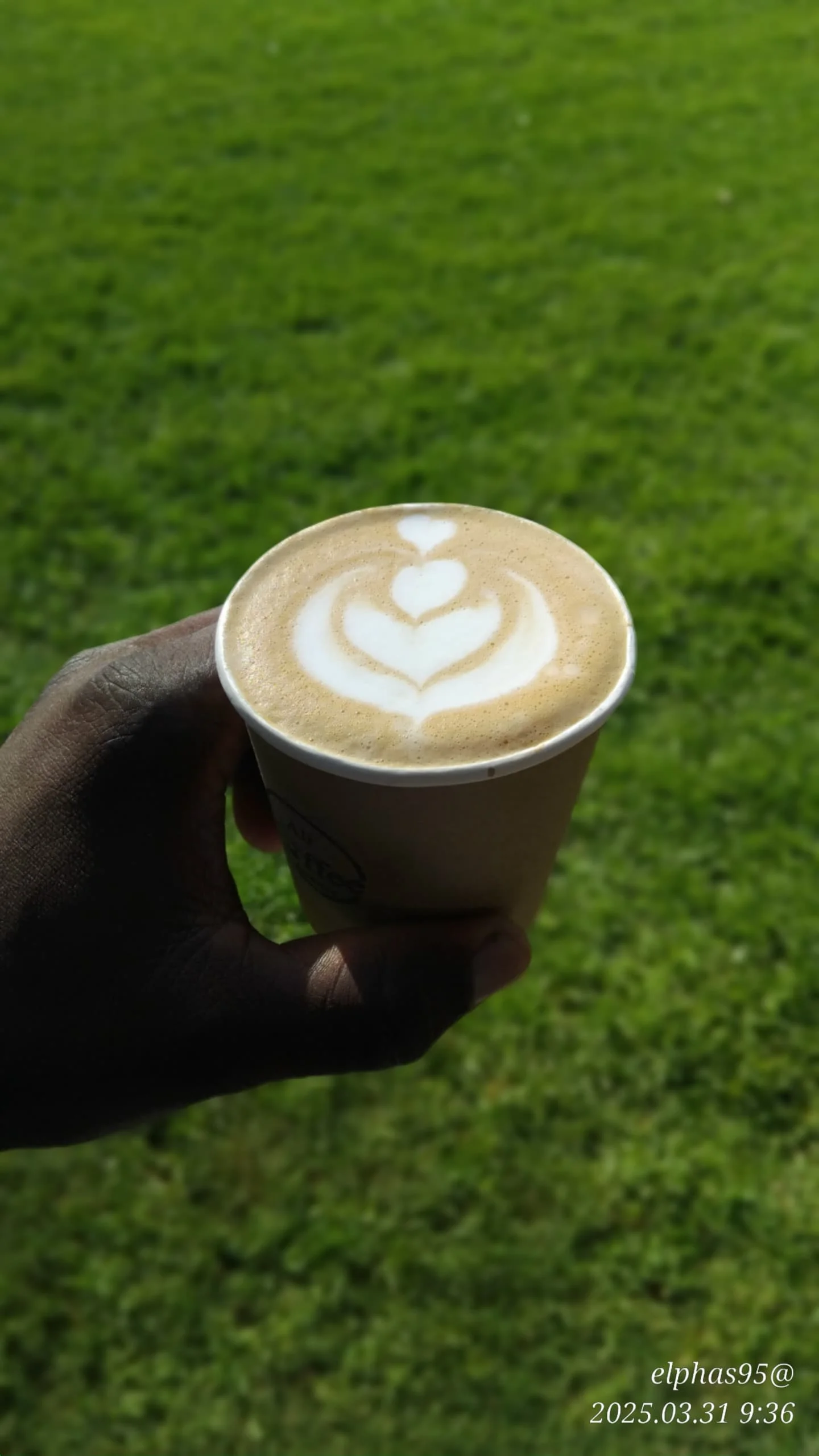 EL-J Coffee takeaway cup on a lush green grass lawn